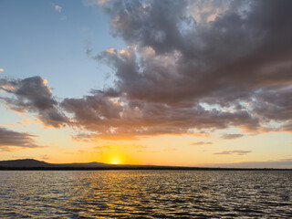 Obraz premium Sunset over a lake with clouds and mountains in the background