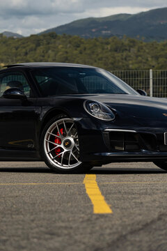 Black Porsche 911 Carrera GTS front wheel and headlight close up, Luxury sports car outdoors external shot