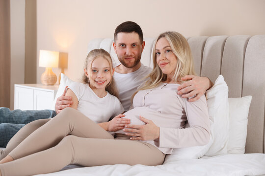 Pregnant woman with her daughter and husband on bed at home