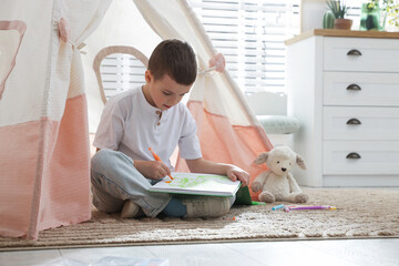Little boy drawing in sketchbook near toy wigwam at home © New Africa