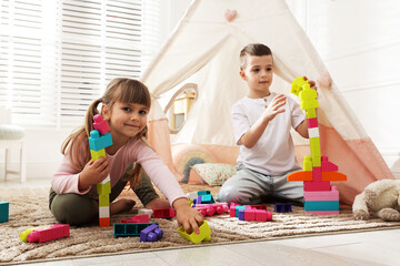 Little kids playing with building blocks near toy wigwam at home © New Africa