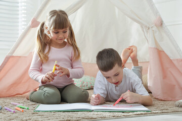 Little kids drawing in sketchbook together near toy wigwam at home © New Africa
