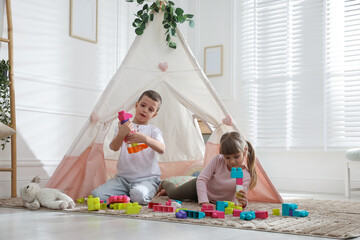 Little kids playing with building blocks near toy wigwam at home © New Africa
