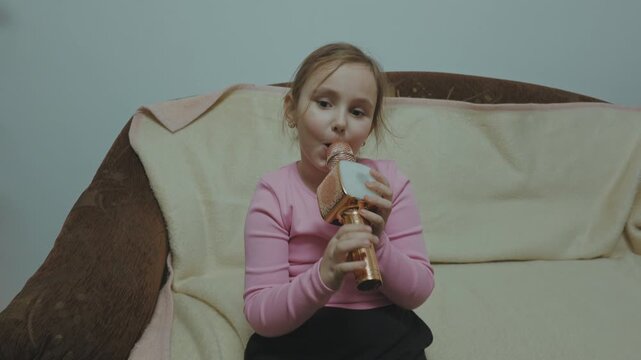 One young girl having fun at home while singing into colorful wireless karaoke microphones during a video recording.