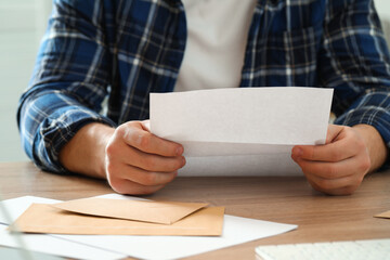 Obraz premium Man reading letter at wooden table indoors, closeup