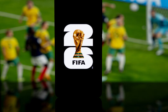 FIFA World Cup 2026 logo and trophy displayed on a smartphone screen with a blurred football match background, international soccer tournament and sports media concept