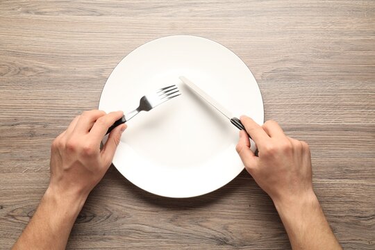 Man with cutlery and plate on wooden table, top view