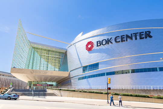 Clean architectural view of the BOK Center featuring its curved glass and metal facade against a clear blue sky in Tulsa, Oklahoma.