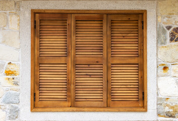 Obraz premium Wooden shutters background of a rustic window with three brown timber louvered panels set in a textured natural stone wall for Mediterranean architectural design.