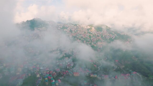Cinematic drone flight through low clouds revealing the densely packed mountain city of Shimla, India.