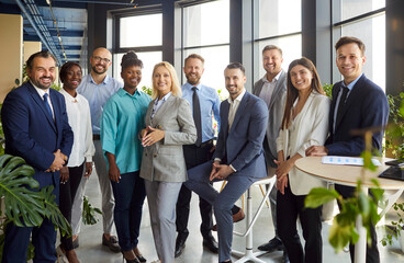 Obraz premium Group portrait of diverse happy business people standing in row after successful business meeting or training. Smiling male and female company employees making group photo and looking at camera.