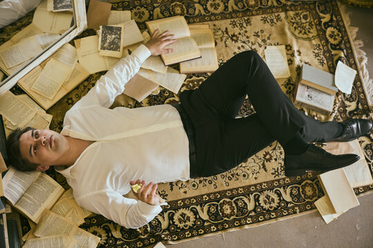Man reclined on decorative carpet examining written pages deeply