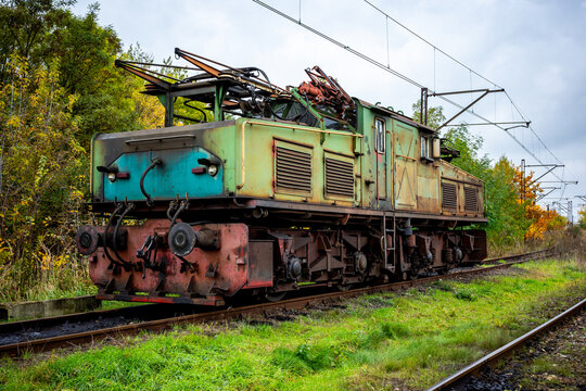 An old, green, electric shunting locomotive standing on a side track. The photo was taken on a cloudy autumn day.