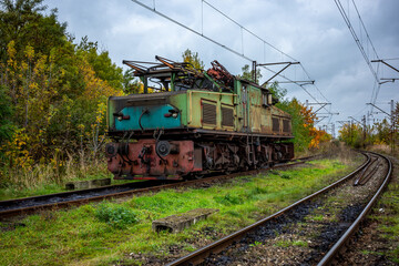 Obraz premium An old, green, electric shunting locomotive standing on a side track. The photo was taken on a cloudy autumn day.