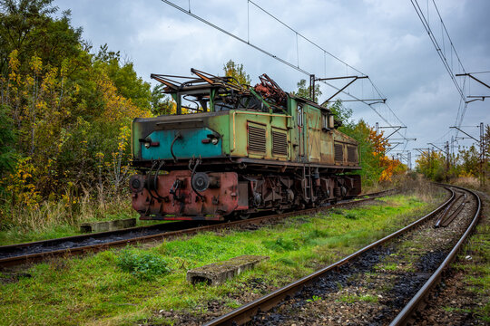 An old, green, electric shunting locomotive standing on a side track. The photo was taken on a cloudy autumn day.