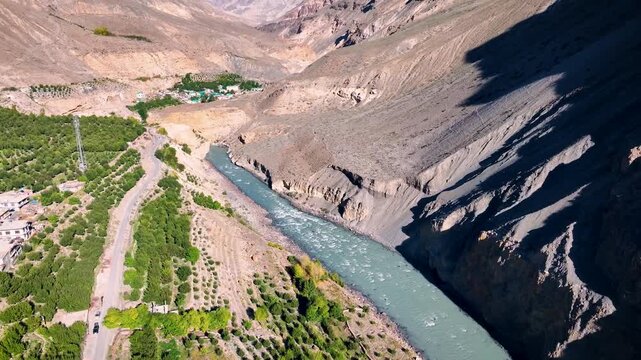 Cinematic aerial Orbit Shot of Lush green high-altitude apple orchard farm on banks of spiti river in Himalayan cold desert, India