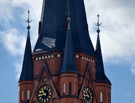 Close view of historic red clock tower with intricate hands and bricked exterior in moody sky setting