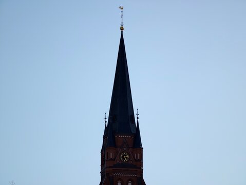 Graceful steeple against azure background. Vertical gothic structure features refined ornament and sharp peak
