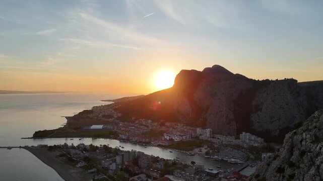 Aerial drone panoramic view of Omis, Croatia with Cetina river, mountains and Adriatic coastline, cinematic landscape of Dalmatian town surrounded by cliffs and sea, beautiful sunset