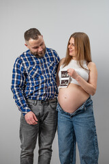 Fototapeta premium Portrait of a pregnant couple holding an ultrasound scan on a gray background.