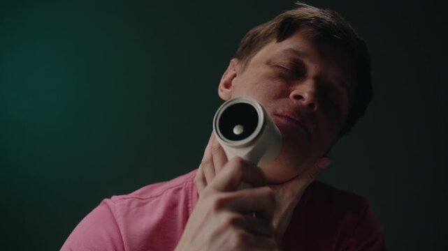 Portrait of cheerful man holding and using electric lint remover to cheek, forehead and neck, creating funny and unconventional self care moment for new personal grooming experience, slow motion.