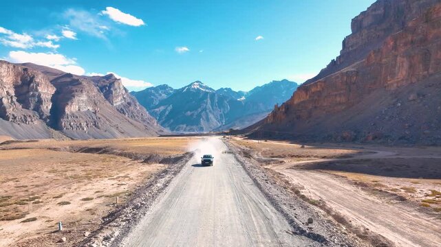 Low-altitude aerial tracking shot of an off-road vehicle navigating the rugged, barren valley floor of Spiti, India.
