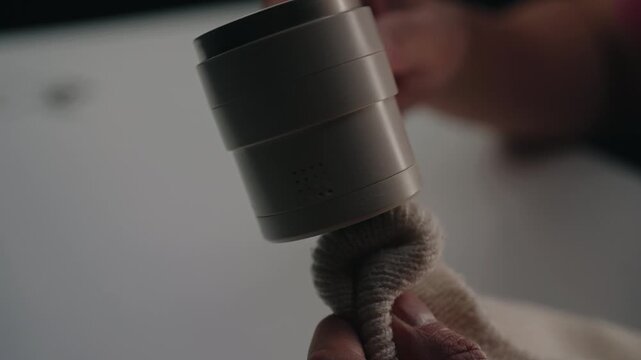 Hands of male using electric lint remover machine on a fabric garment, carefully eliminating pilling and fuzz for renewed textile care and maintenance, close-up, slow motion.