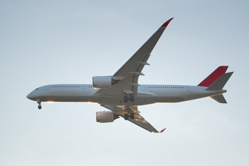 Obraz premium Close side profile of a passenger airplane with extended landing gear, illuminated by warm sunlight, highlighting aerodynamic design, aviation engineering, and global air transport.