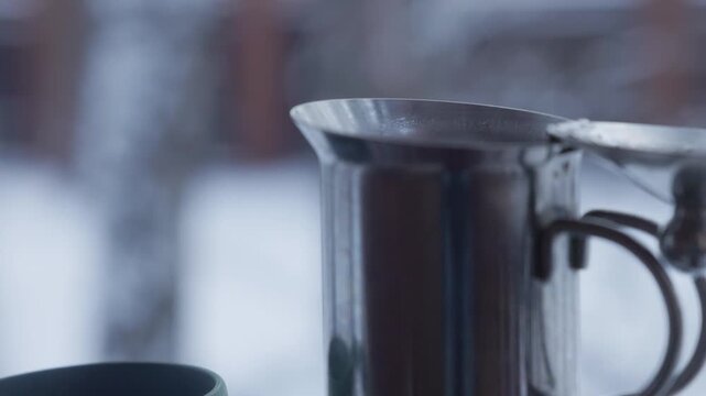 Morning light glimmers on a silver pot as warm coffee wafts into a cozy mug, ideal for a chilly snowy day.
