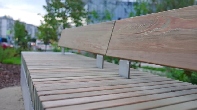 Bench with wooden planks in summer urban park closeup. Empty clean seat near flowerbed on city street. Place to rest in public garden