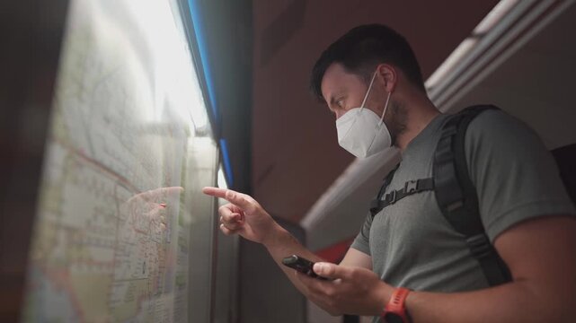 Allergy sufferer in a face mask looking at the timetable in Munich U-Bahn. Using a mobile app to navigate public transport during a strike day. Navigation bei Zugausfaellen in Deutschland