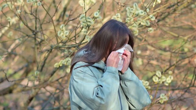 Young Woman Sneezing and Blowing Nose into Tissue in Spring Forest Allergy Reaction to Tree Pollen