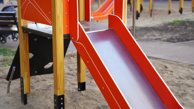 Orange playground slide stands between wooden supports. Smooth ramp leads down from platform shaping active play route in modern yard