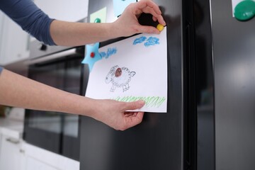 Naklejka premium Woman putting child's drawing onto refrigerator indoors, closeup