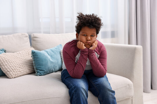 Portrait of resentful little boy sitting on sofa at home