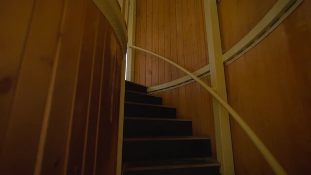 Wooden tower interior shows small room and curved stairway. Dark steps lead upward inside play structure inviting kids climbing activities