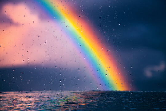 A vibrant rainbow appears in the sky over a body of water after a rainstorm