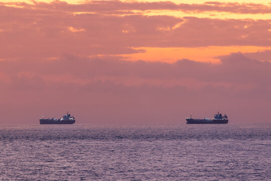 Tanker ships with oil floating idle on calm ocean horizon at sunset, waiting for channel strait unblocking
