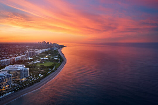 Aerial view of a coastal city at sunset with a vibrant sky and calm ocean waters
