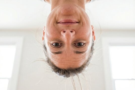 Upside down portrait of a smiling woman looking directly at the camera in a bright room
