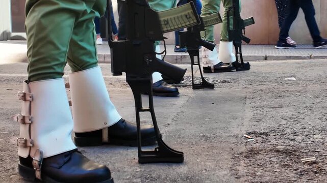 Row of military soldiers standing in formal formation wearing green uniforms and white gaiters during official ceremony parade on urban street