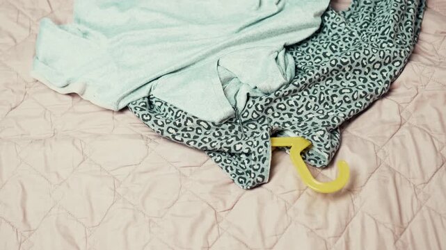 Decluttering process: Woman taking clothes on hangers out of wardrobe and putting them on a bed, top view,4k 10-bit footage.