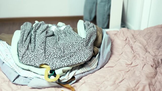 Decluttering process: Woman taking clothes on hangers out of wardrobe and putting them on a bed,4k 10-bit footage.