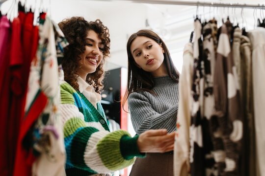 Happy young women choosing clothes in trendy boutique