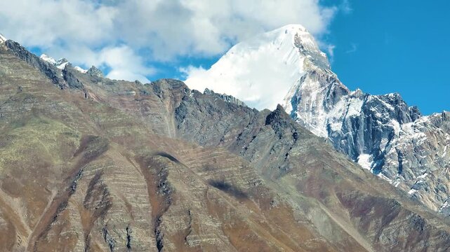 Cinematic camera tilt up revealing a massive, pristine snow-capped mountain peak in Chitkul, India.