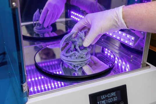 Gloved hand placing a 3d printed resin dragon model into a uv light curing station