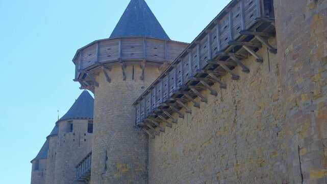 Stone fortress towers and walls with wooden battlements under blue sky