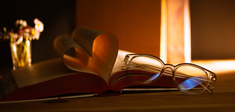 Reading opens the heart with a book that has pages shaped like a heart and glasses beside it, showing a moment of love for literature and knowledge in a cozy setting
