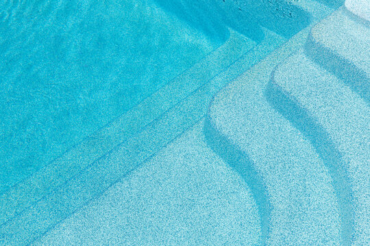 New modern fiberglass plastic swimming pool entrance step with clean fresh refreshing blue water on bright hot summer day at yard or resort hotel spa area. Wooden flooring deck of teak or larch board
