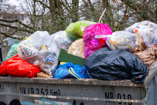 Overflowing metal dumpsters filled with plastic trash bags, outdoor waste disposal area, garbage collection point, municipal waste management, pollution nature, household waste disposal in Europe